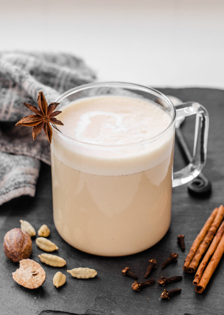 A mug of copycat Starbucks chai tea latte on a dark background with chai spices around it.