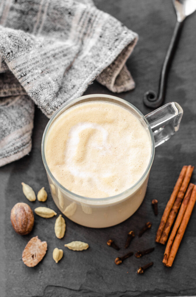 A mug of copycat Starbucks chai tea latte on a dark background with chai spices around it.