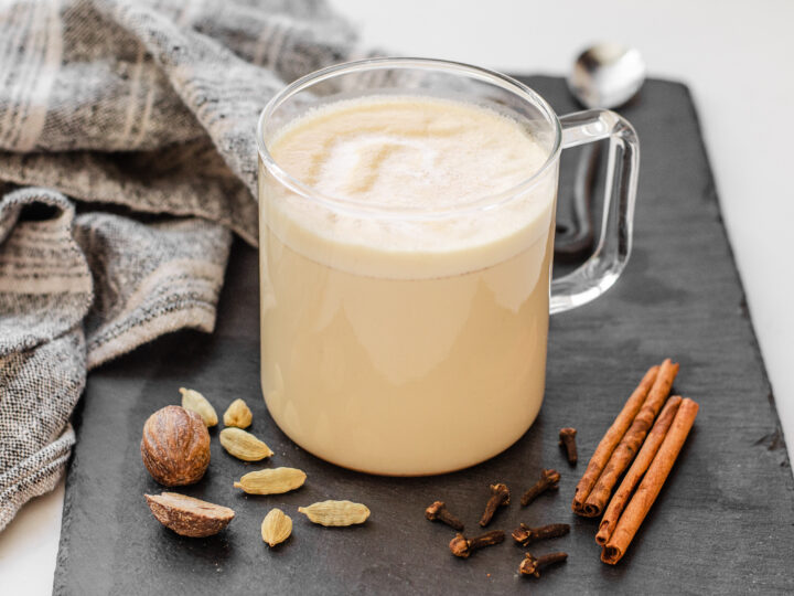 A mug of homemade Starbucks chai tea latte on a slate board with spices around it and a tea towel to the side.