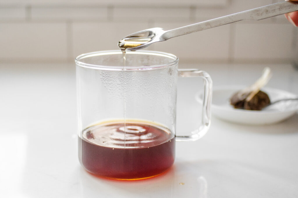 Adding maple syrup to the steeped chai tea in the mug.