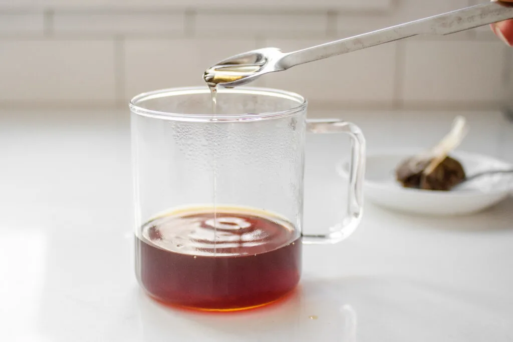 Adding maple syrup to the steeped chai tea in the mug.