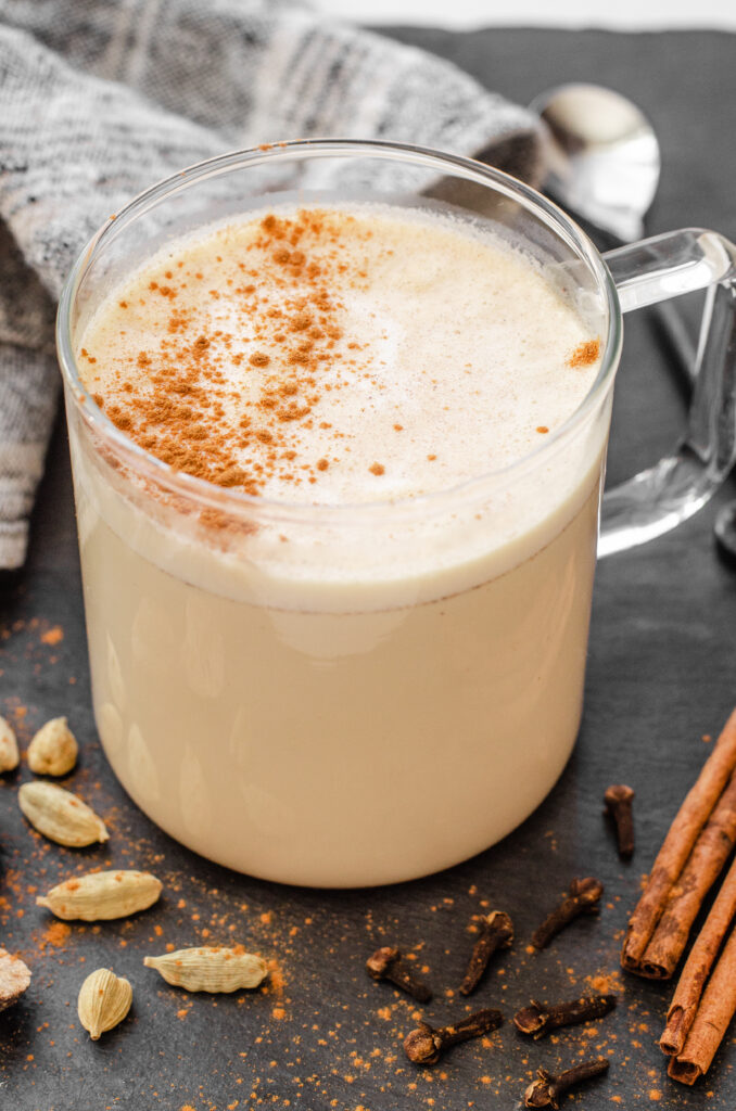 A mug of masala chai with spices all around it.