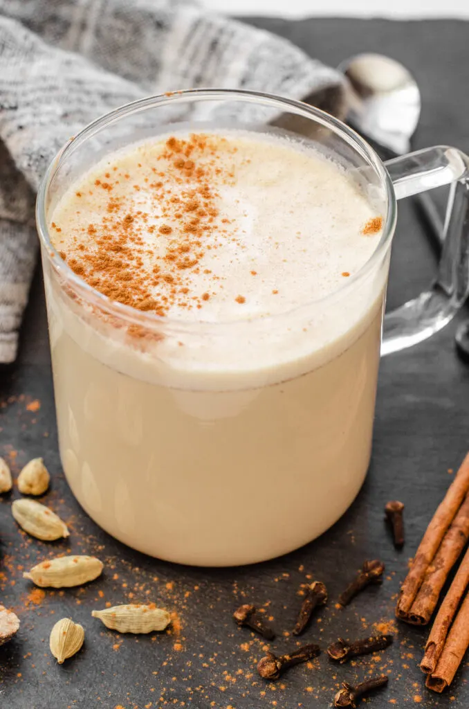 A mug of masala chai with spices all around it.