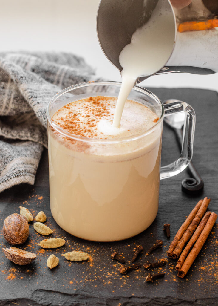 Pouring frothed milk into a mug to make a copycat Starbucks chai tea latte with spices around the mug.