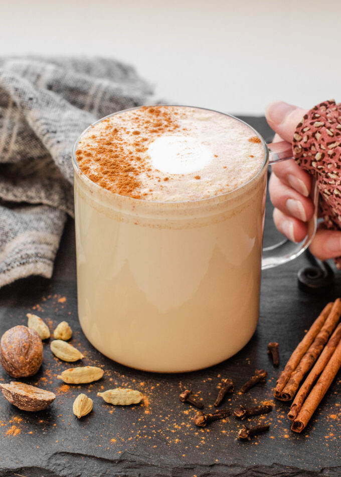 Holding a mug of copycat Starbucks Chai Tea Latte on a dark background with spices around it.