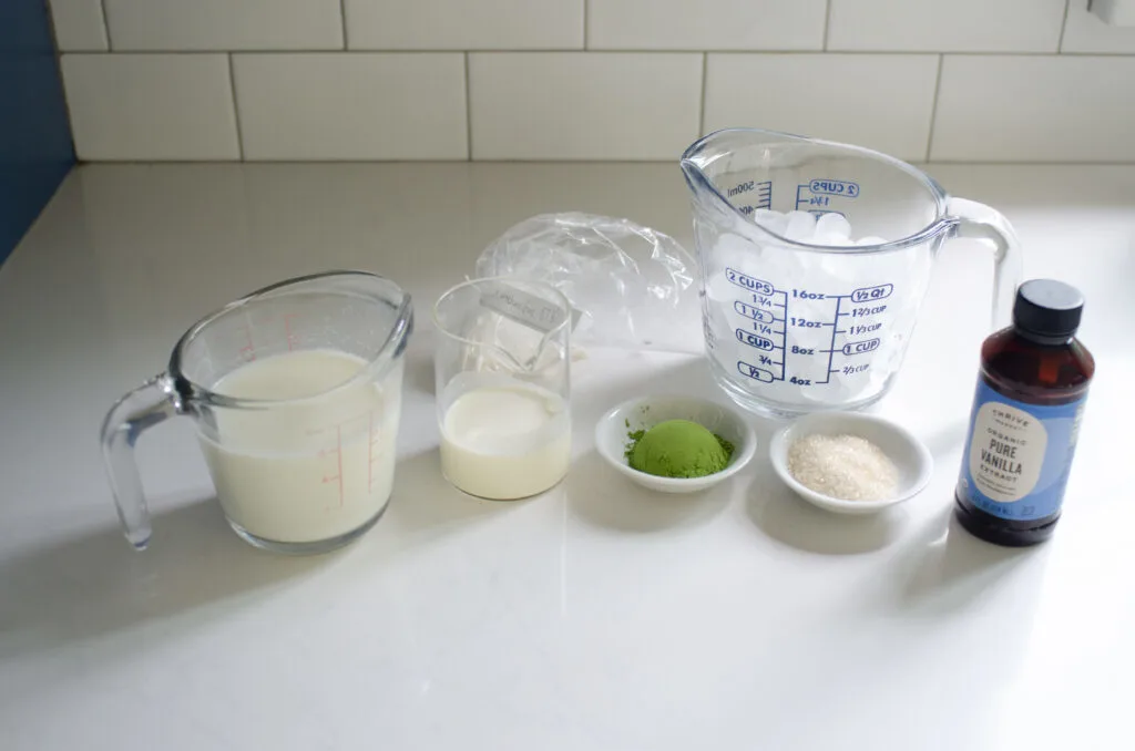 All of the ingredients needed to make a Starbucks Matcha Green Tea Frappuccino at home laid out on a white countertop.