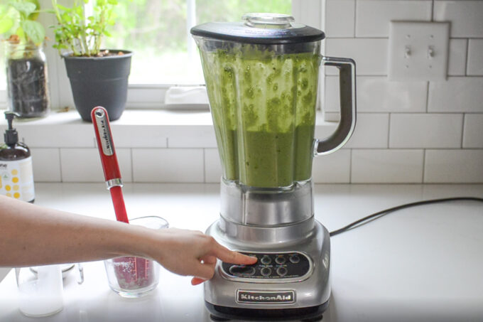 A clear glass filled with a matcha Frappuccino with a hand holding it on the left.