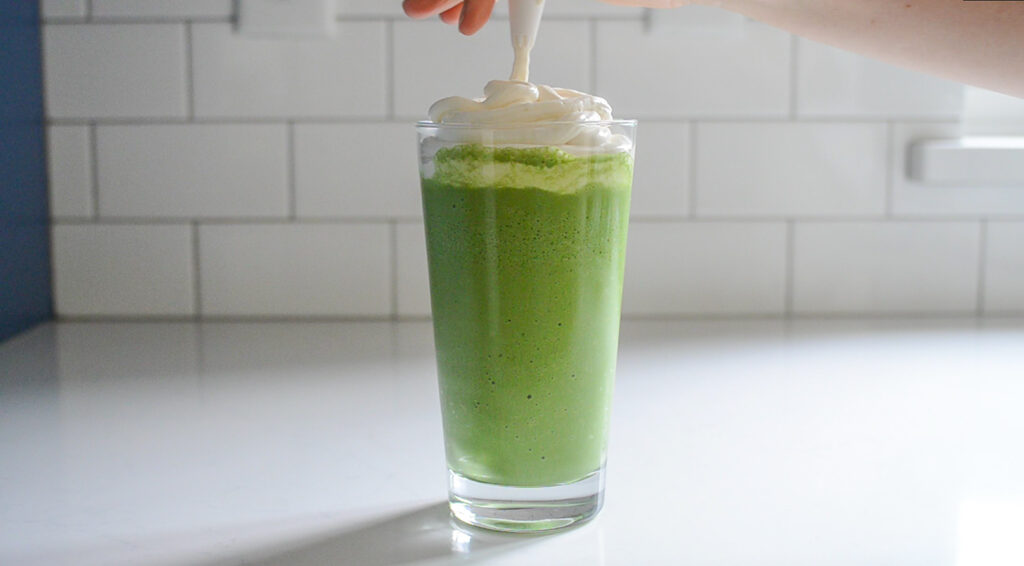 Piping the whipped cream on top of the green tea frappe. 