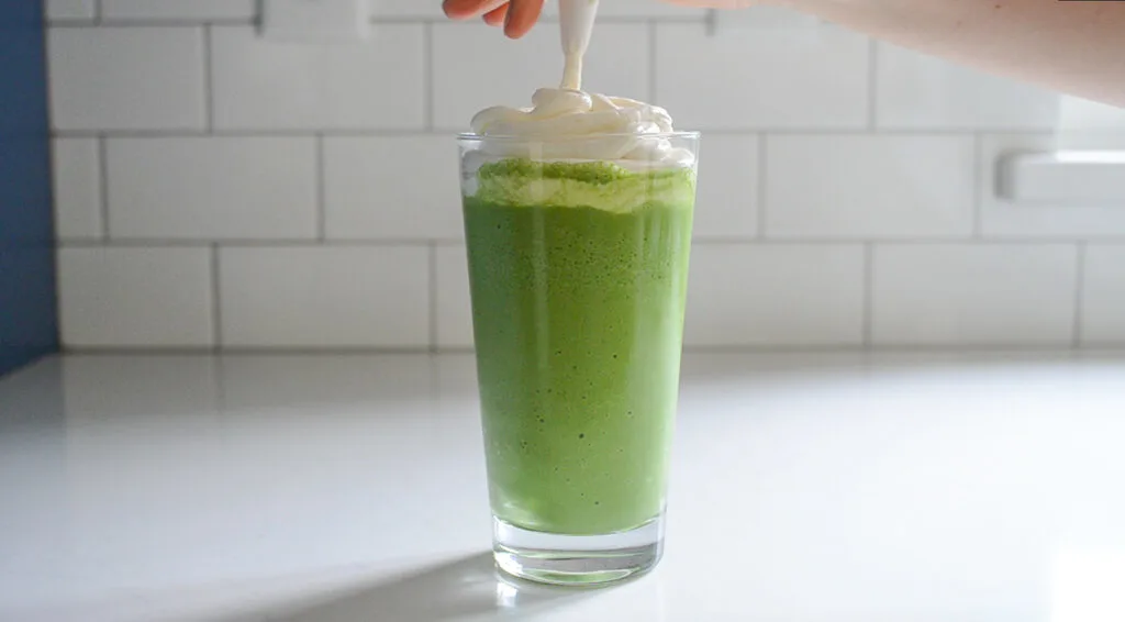 Piping the whipped cream on top of the green tea frappe. 