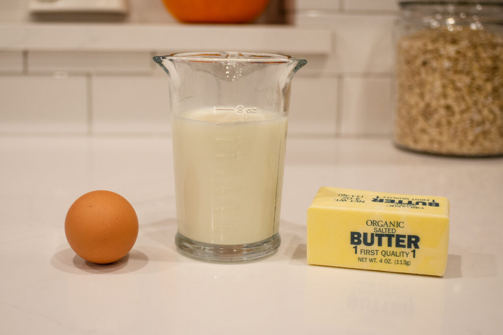 Butter, an egg, and milk on a countertop for making an enriched sourdough sandwich bread.