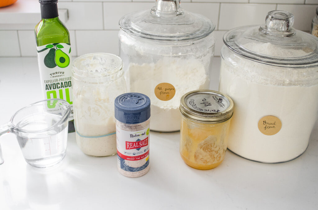 All of the ingredients needed to make a soft sourdough sandwich bread laid out on a white countertop.