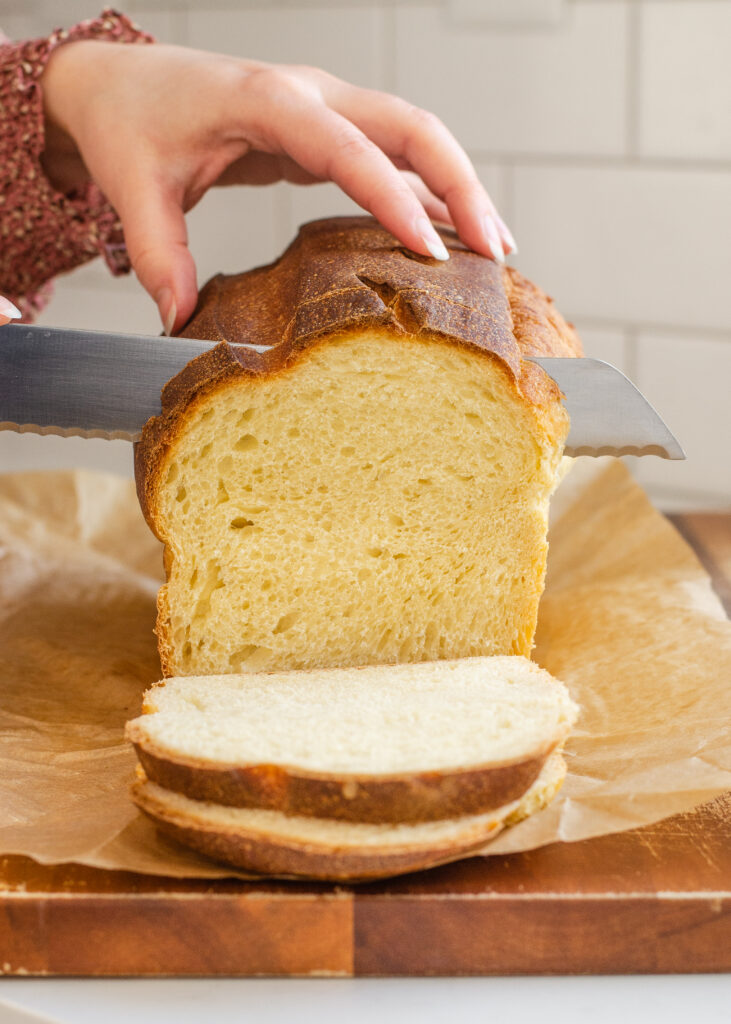 Slicing a loaf of sourdough sandwich bread on a wooden cutting board.