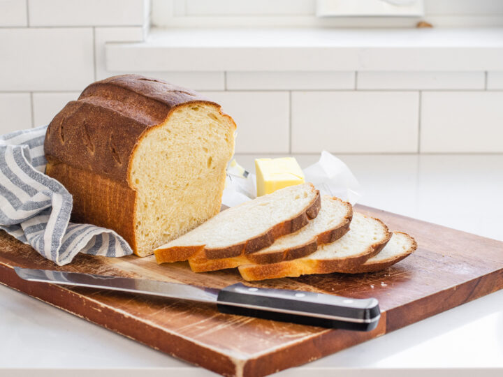 A loaf of sourdough sandwich bread with a few slices on a wooden cutting board.