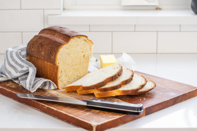 A loaf of sourdough sandwich bread with a few slices on a wooden cutting board.