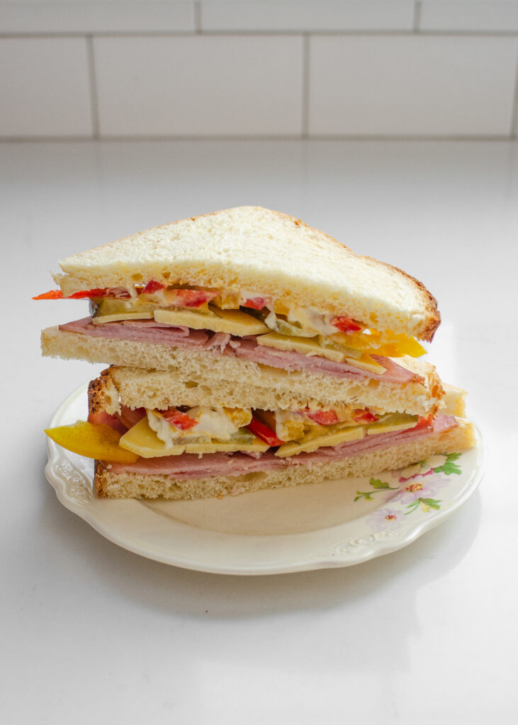 A sandwich made with sourdough sandwich bread on a vintage plate on a white countertop.