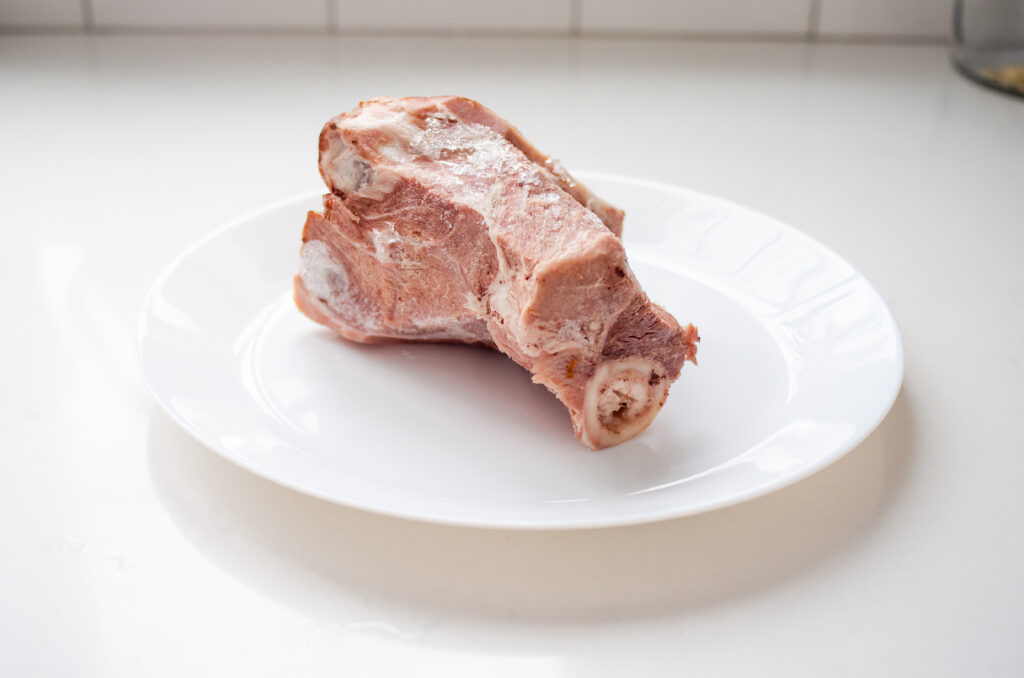 A ham bone on a white plate on a white countertop.