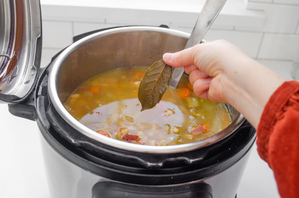 Removing the bay leaf from the ham and bean soup before serving.