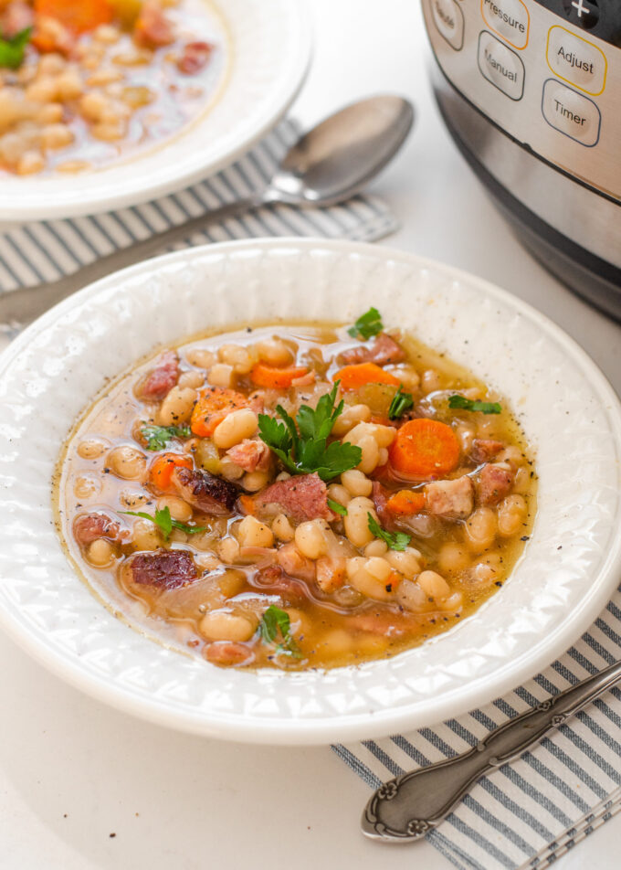 Close up shot of a bowl of ham and bean soup on a white countertop with the Instant Pot in the background.