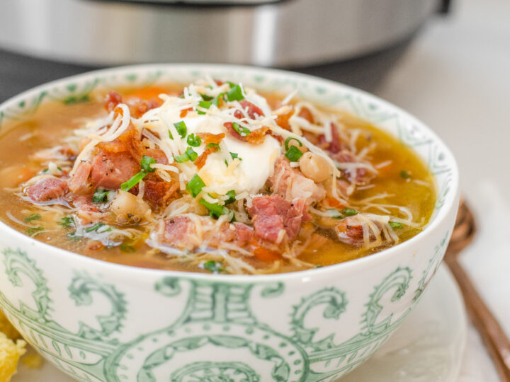 A bowl of ham and bean soup on a plate with cornbread off to the side and the Instant Pot in the background.