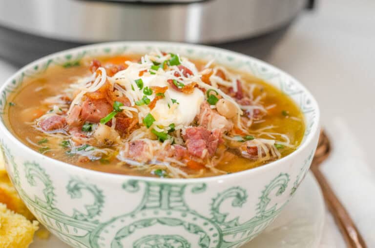 A bowl of ham and bean soup on a plate with cornbread off to the side and the Instant Pot in the background.