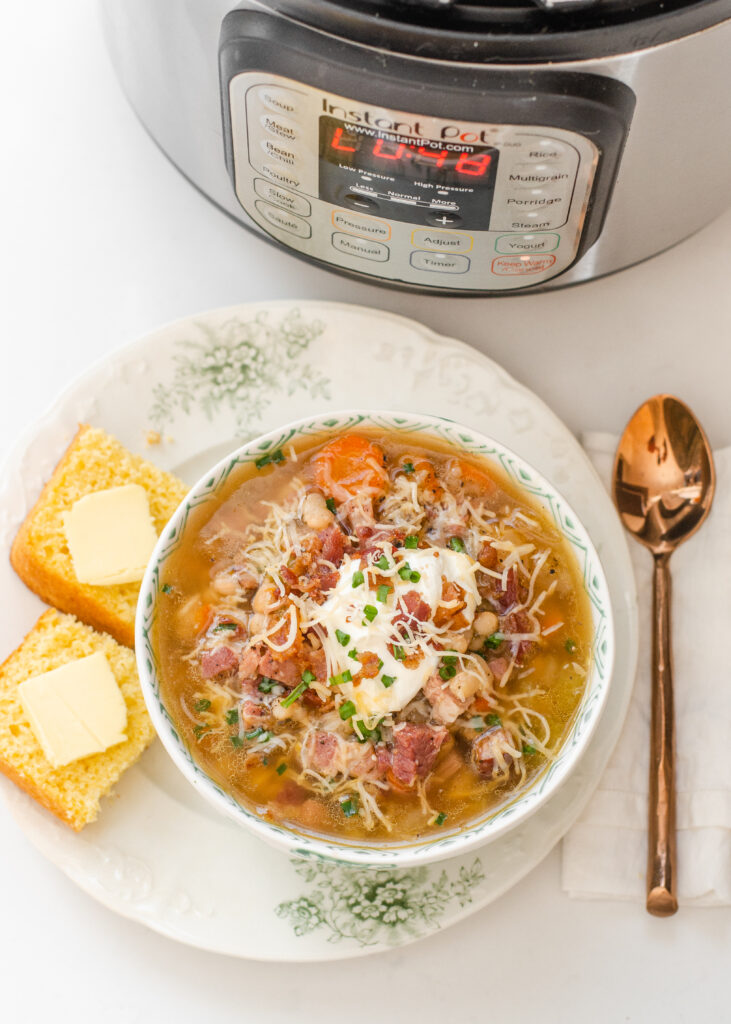 A bowl of ham and bean soup on a plate with cornbread off to the side and the Instant Pot in the background.