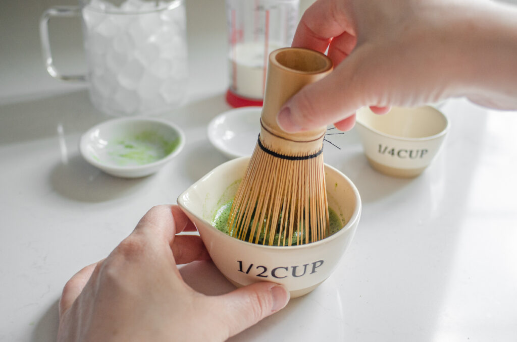 Whisking the matcha powder with water in a small bowl with a bamboo matcha whisk.