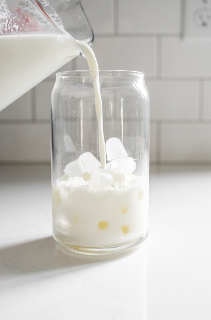 Adding milk on top of the ice in a glass.