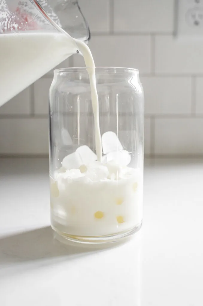 Adding milk on top of the ice in a glass.