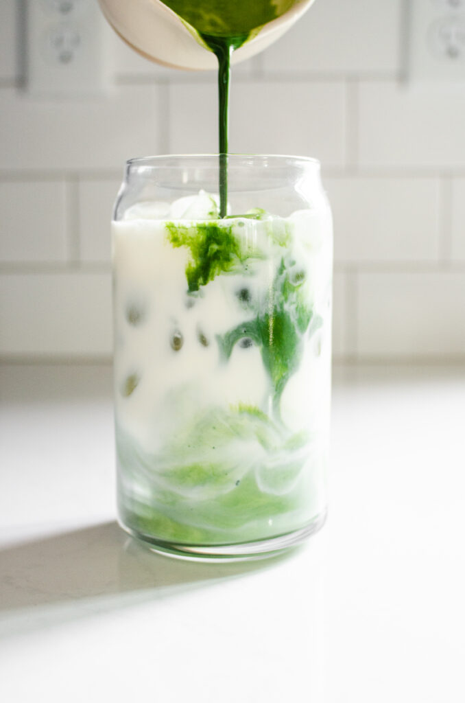 Pouring the matcha mixture on top of the ice and milk in the glass.