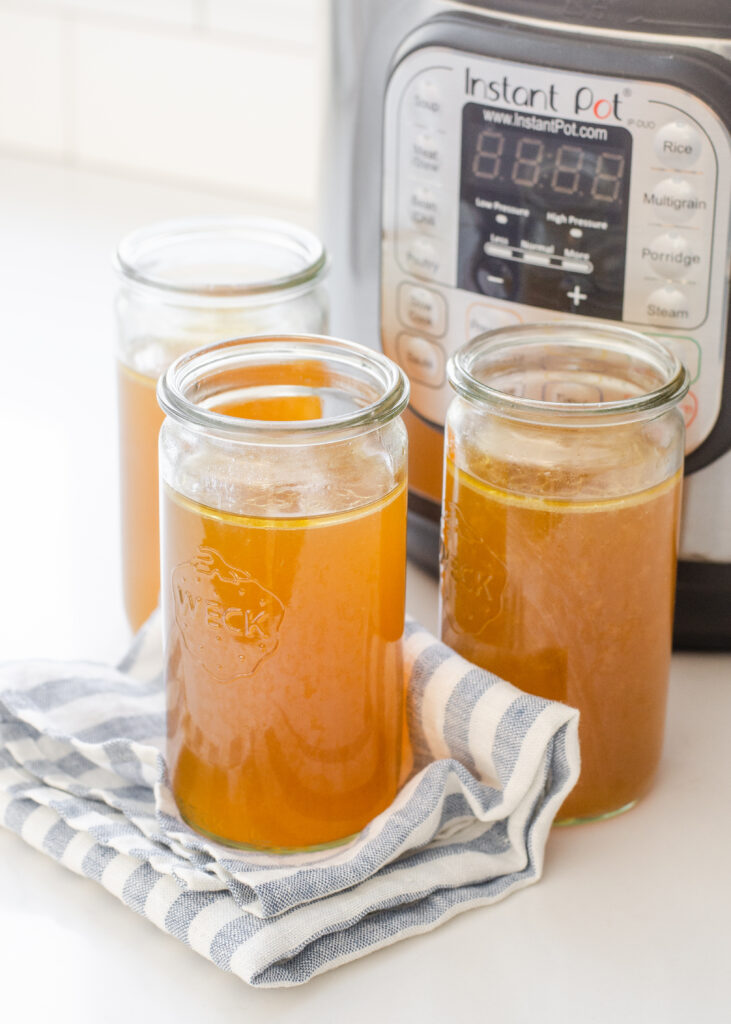 Weck jars filled with homemade chicken bone broth with the Instant Pot behind them.