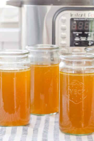 Weck jars filled with homemade chicken bone broth with the Instant Pot behind them.