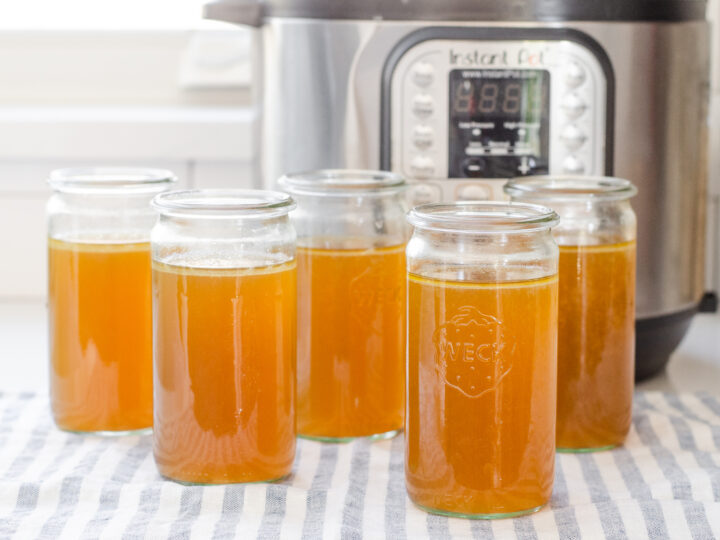 Weck jars filled with homemade chicken bone broth with the Instant Pot behind them.