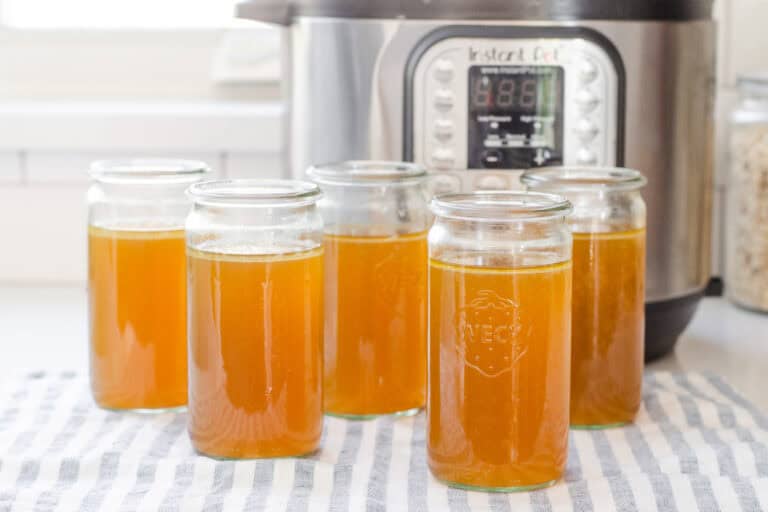 Weck jars filled with homemade chicken bone broth with the Instant Pot behind them.