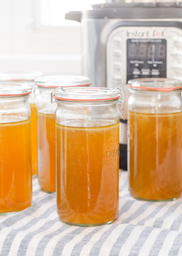 Weck jars filled with homemade chicken bone broth with the Instant Pot behind them.