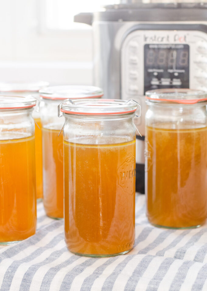 Weck jars filled with homemade chicken bone broth with the Instant Pot behind them.