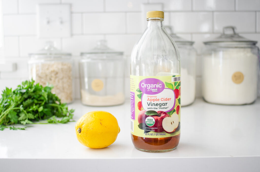 A lemon and apple cider vinegar on a white countertop.