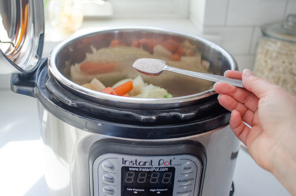 Adding salt to the chicken bone broth in the Instant Pot.