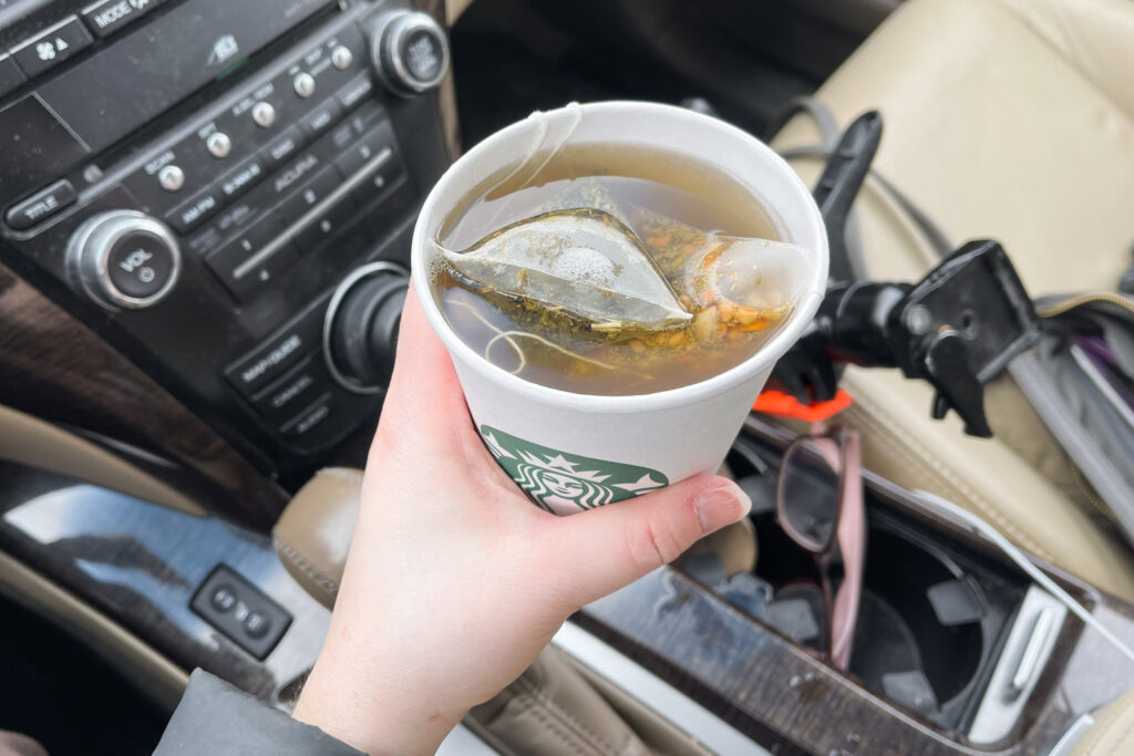 A hand holding the Starbucks medicine ball tea, AKA honey citrus mint tea in a car.