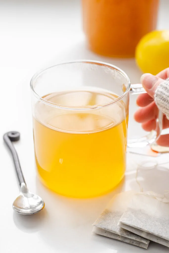 A mug of Starbucks medicine ball tea with a spoon on one side, tea bags on the other, and a lemon behind it.