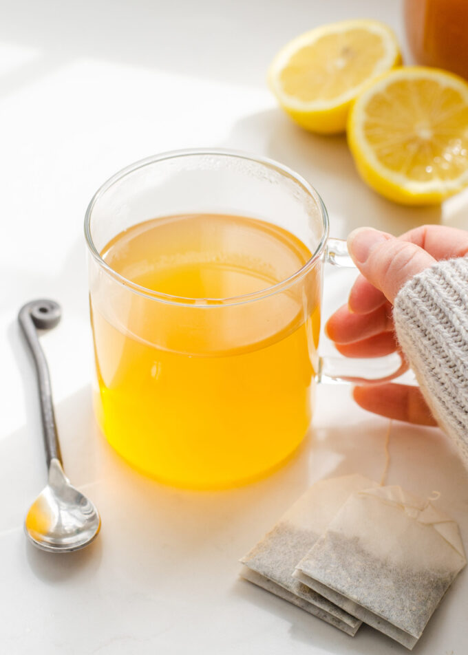 A mug of Starbucks medicine ball tea with a spoon on one side, tea bags on the other, and a lemon behind it.