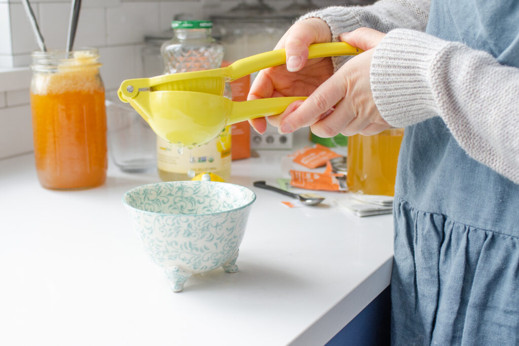 Squeezing lemon juice into a mug on a white countertop with ingredients in the background.
