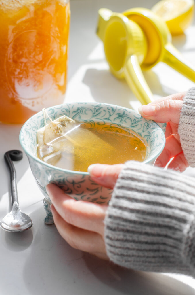 Hands holding a mug of Starbucks medicine ball tea with ingredients in the background.