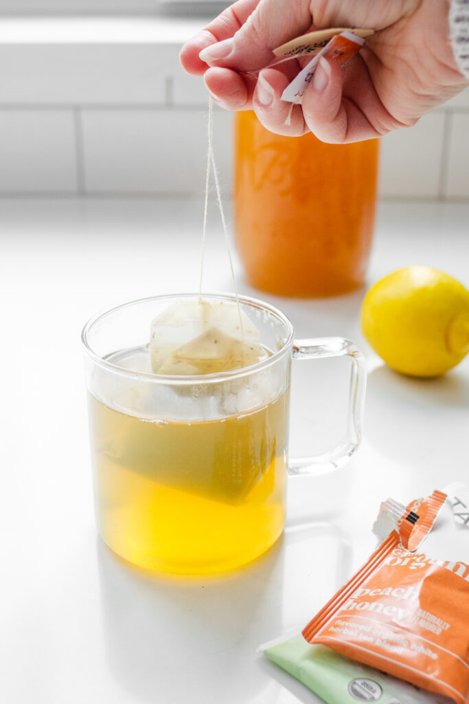 A mug with the makings of the Starbucks medicine ball tea with the tea bag wrappers in the foreground and a hand holding the strings of the tea bags.