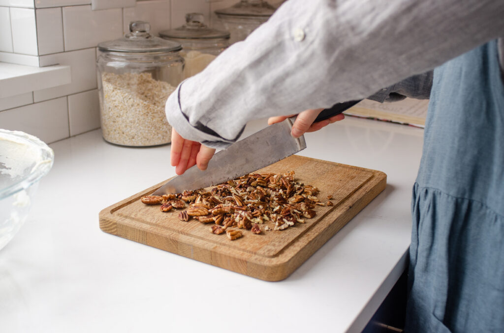 Chopping toasted pecans on a wooden cutting board with a chef's knife.