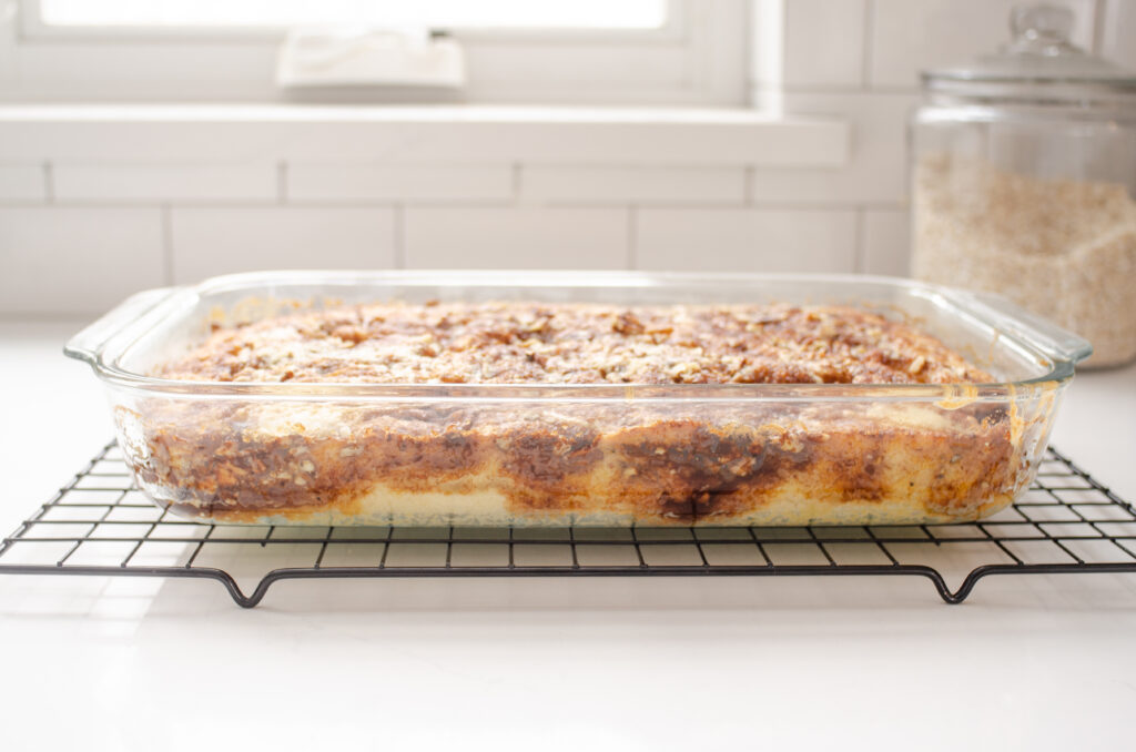A baked pan of sourdough coffee cake cooling on a wire cooling rack on a white countertop with a window in the background.