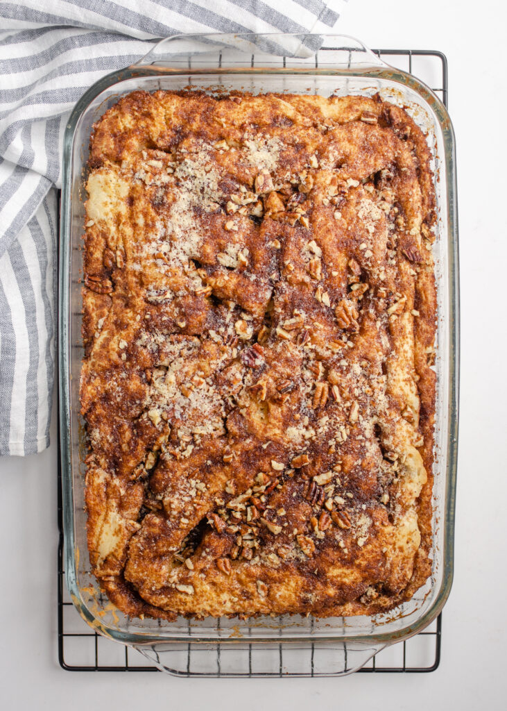 A pan of sourdough coffee cake made with cinnamon and pecans on a wire cooling rack with a linen tea towel in the background.