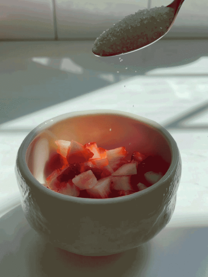 Adding sugar to chopped strawberries to macerate for a strawberry matcha latte.
