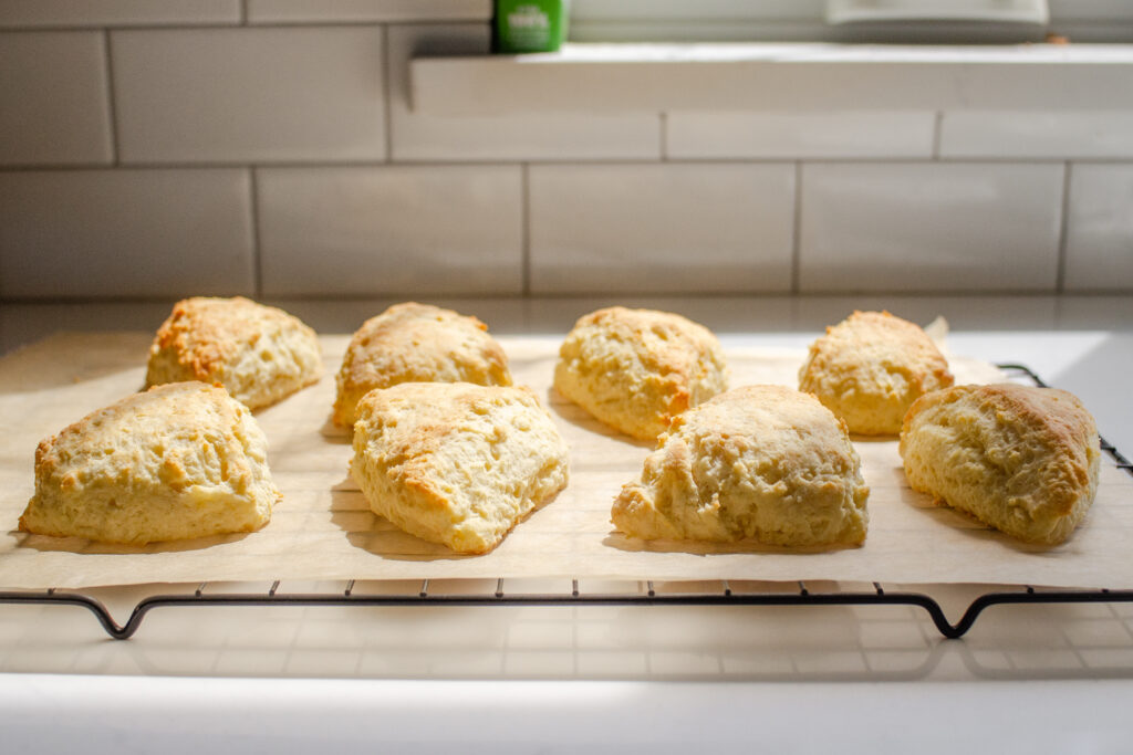 Lemon scones on a piece of parchment paper on a wire cooling rack with the sunshine coming through a window.