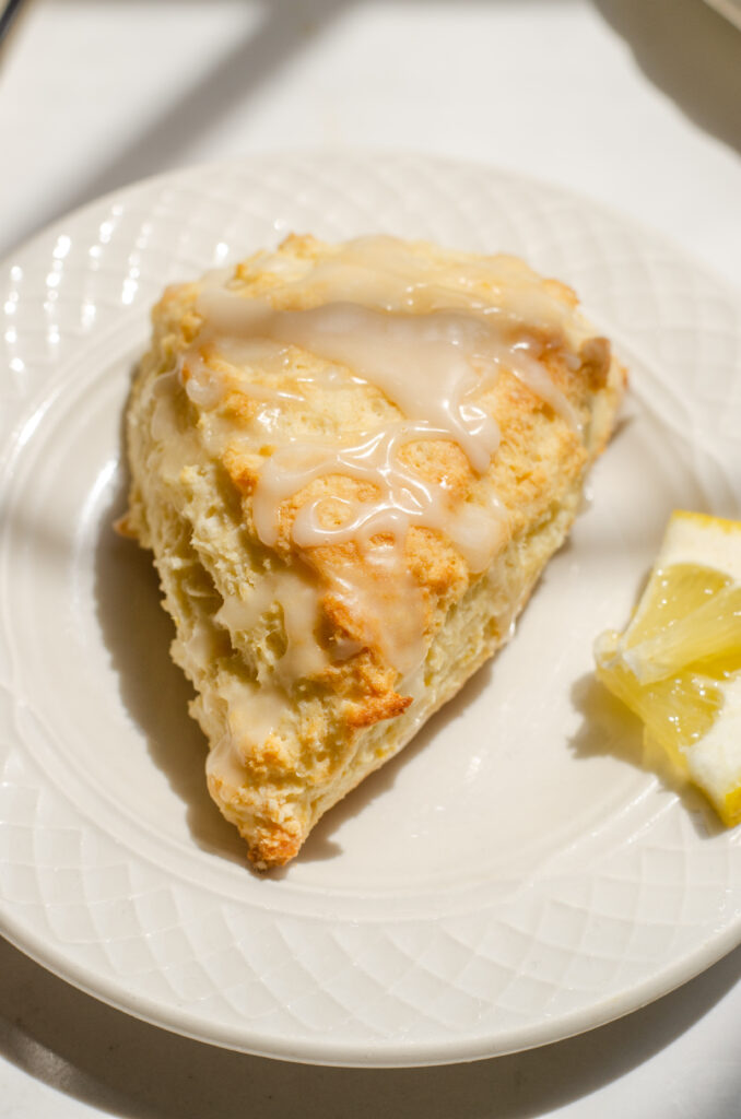 A lemon scone on a plate with small slices of lemon next to it.