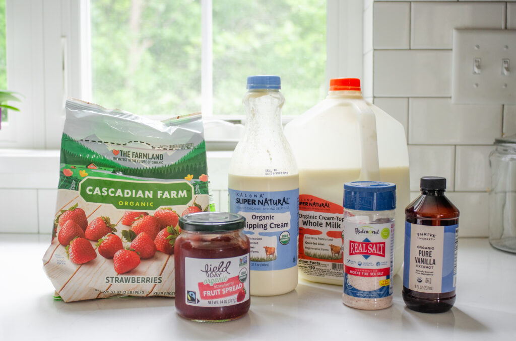 All of the ingredients needed to make a strawberry milkshake without ice cream laid out on a white countertop with a window in the background.